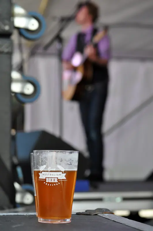 A cup of GABF beer on stage with an out of focus Bob Evans in the background