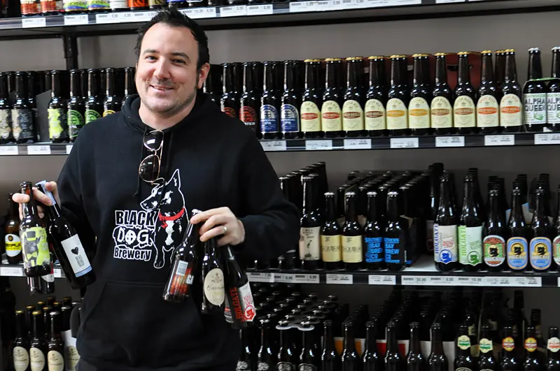 Mark Iscaro holds craft beer bottles in front of shelves of beer
