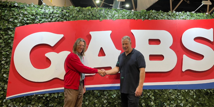 Jerry Schwartz & Mike Bray shaking hands in front of a red GABS sign