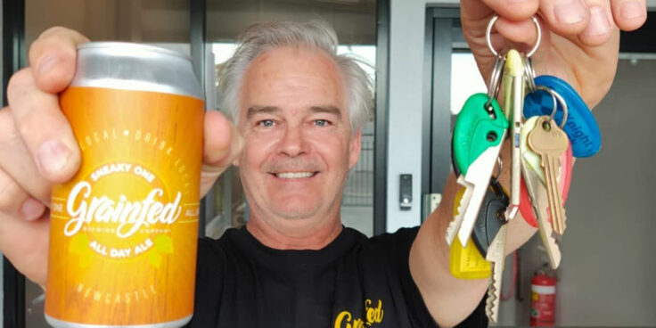 Lachlan McBean holding a beer and keys to his new Grainfed Brewing venue (cropped)