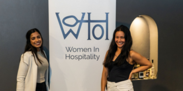 Women standing on either side of a Women In Hospitality sign
