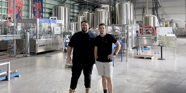 Two men standing in front of brewing equipment