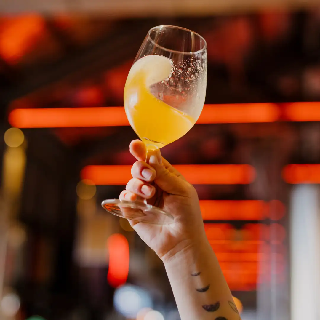 Glass of Sirens’ Haze 2.0 by Felons Brewing Co. being held in the air